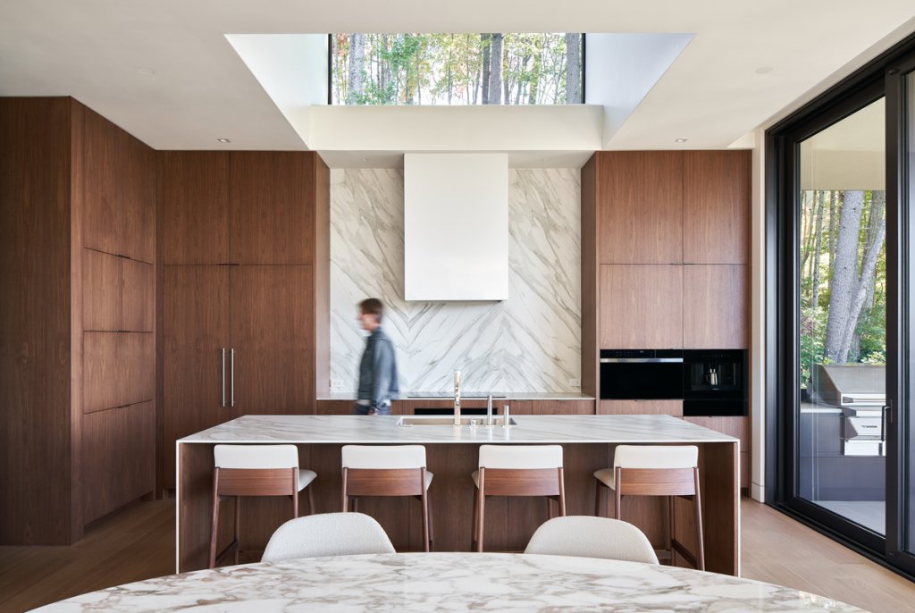 In contrast to the rest of the home’s white-walled interiors, the kitchen features mahogany-stained floor-to-ceiling cabinetry. The kitchen expands into a sitting room that overlooks the mountain range, allowing for a cozy, but impressive, living space.