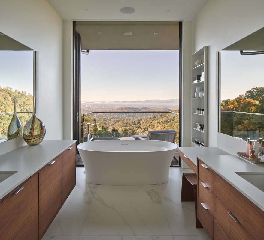 The kitchen’s darker finish flows into an expansive bathroom; its focal point, a large soaking tub, sits in front of an expansive window wall that opens to a deck overlooking the mountains. Parallel vanities create a complementary feeling of symmetry.