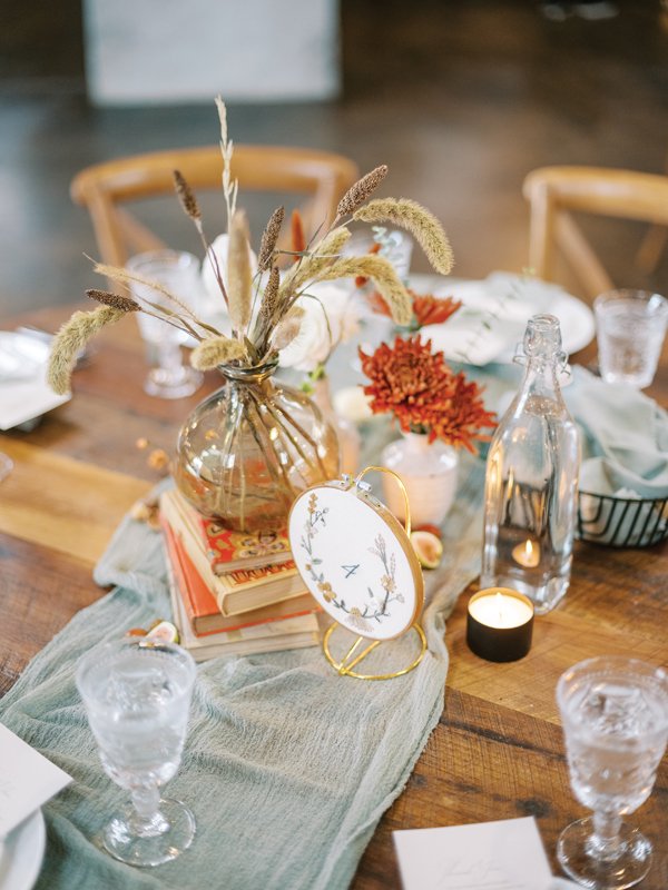 Embroidered table numbers, vases filled with wispy stems in seasonal browns set atop vintage books make for a warm, homespun feel.