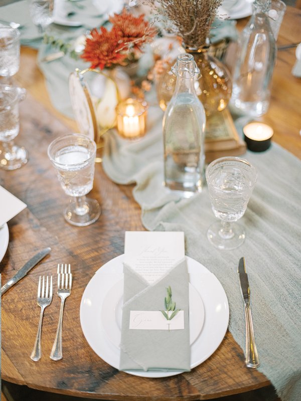 A crisp napkin fold encases menu cards for the evening with delicate greenery stems tucking in each guests name card.