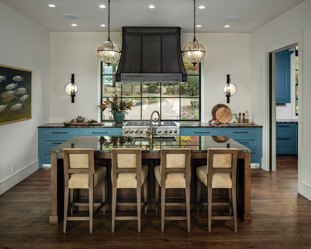 The deep blue cabinet color “screams water,” says Baker, who pulled coordinating shades from the blue veining in the countertops. The windows in the kitchen area also feature dark paneling to create a cozier feel to the oversized glass.