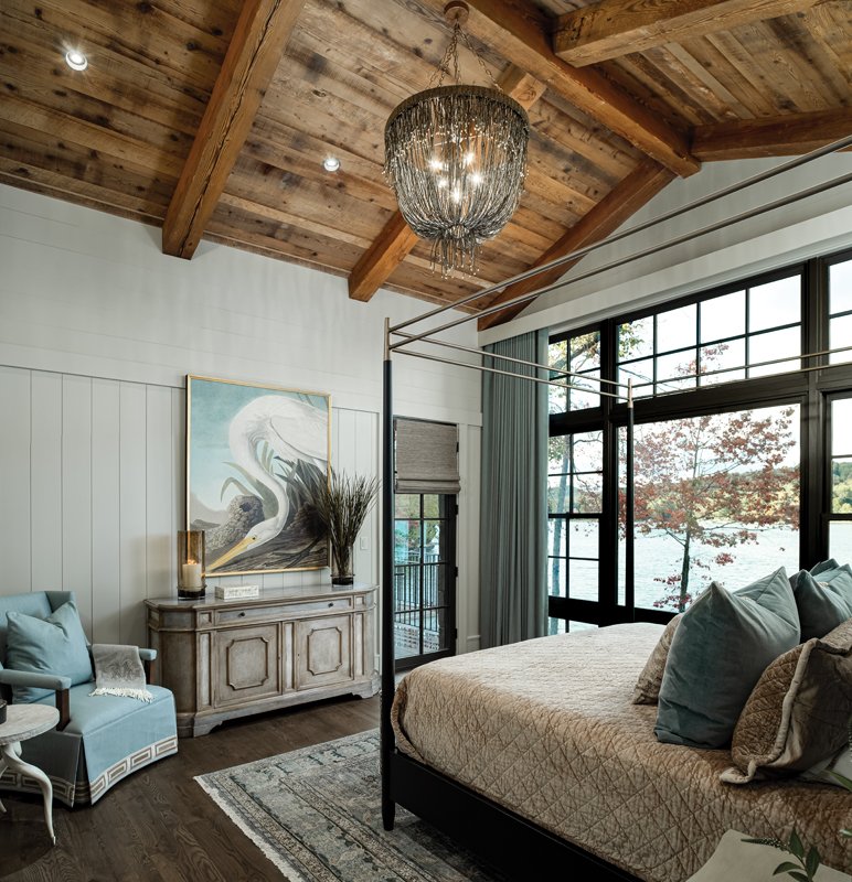 A lighter, softer blue accents the bedroom; from the curtains and linens to the wall art, the shade provides a pop of color to the calming beiges, browns, and whites of the space. A contemporary chandelier sits above the canopy bed, which adds a touch of opulence to the coastal-inspired decor.