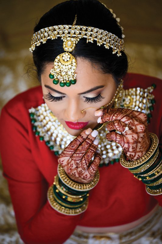 The bride adorns herself with jewels, showcasing her hands with intricate henna.
