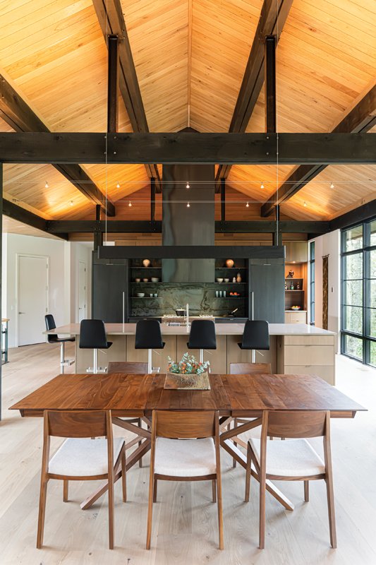 The lighting in the dining room and kitchen area is subtle, so as not to create a visual barrier between the two spaces. It blends into the ceiling beams, which are designed to look aged rather than painted black.