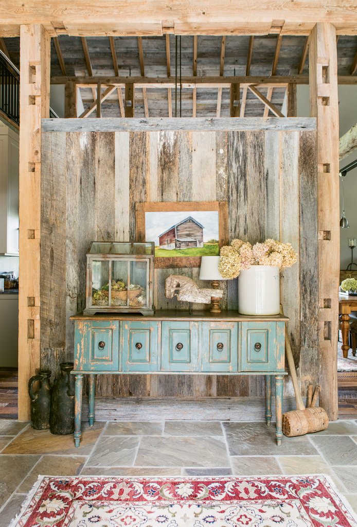 In the entry, a painting showing the original barn (far left) hangs above a rustic side table. A wooden mallet, called a beetle, rests against it, and was used to drive together the mortise and tenon joinery.