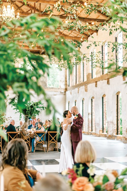 The couple share their first dance while guests look on under a ceiilng draped with greenery.