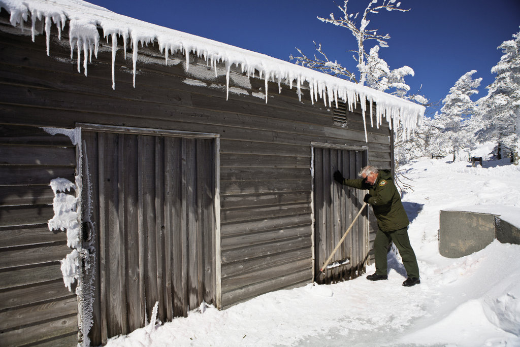 Larry Blevins scrapes away snow to dislodge a frozen door on a gear shed.