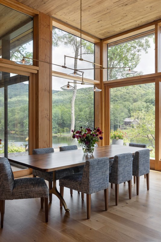 The dining room’s fabric dining chairs were selected to pair with the blue tile backsplash in the kitchen. The open window concept allows the lake view to peer into the dining space. The walnut dining table is made-to-order from Bricker &amp; Beam, and features unique wishbone-shaped legs.