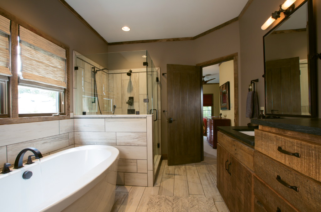 In the master bathroom, long, light color tiles lengthen and brighten the floors, half wall, and shower. A soaking tub replaced an outdated Jacuzzi, and a new vanity was constructed at the WSM Craft Shop from the best specimens of reclaimed wood.