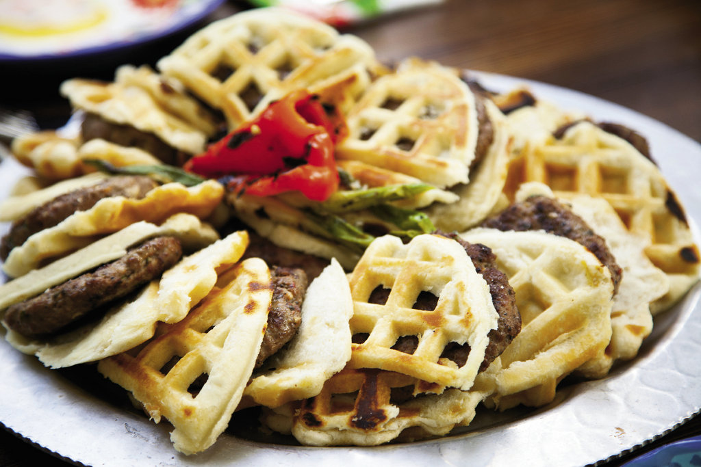 Spicy lamb burgers receive the breakfast treatment with a biscuit waffle bun. Toppings include grilled halloumi cheese, grilled peppers, mustard grilled red onions, pickled beets, and a maple aioli.